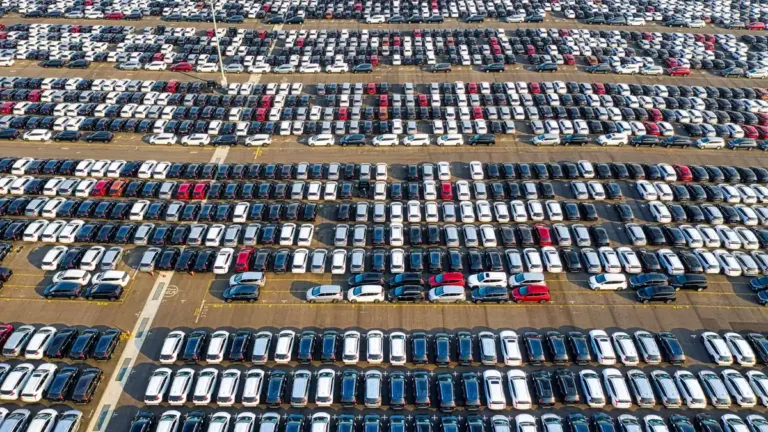 Aerial view of long rows of parked white, silver, blue and dark cars of different sizes on an open lot