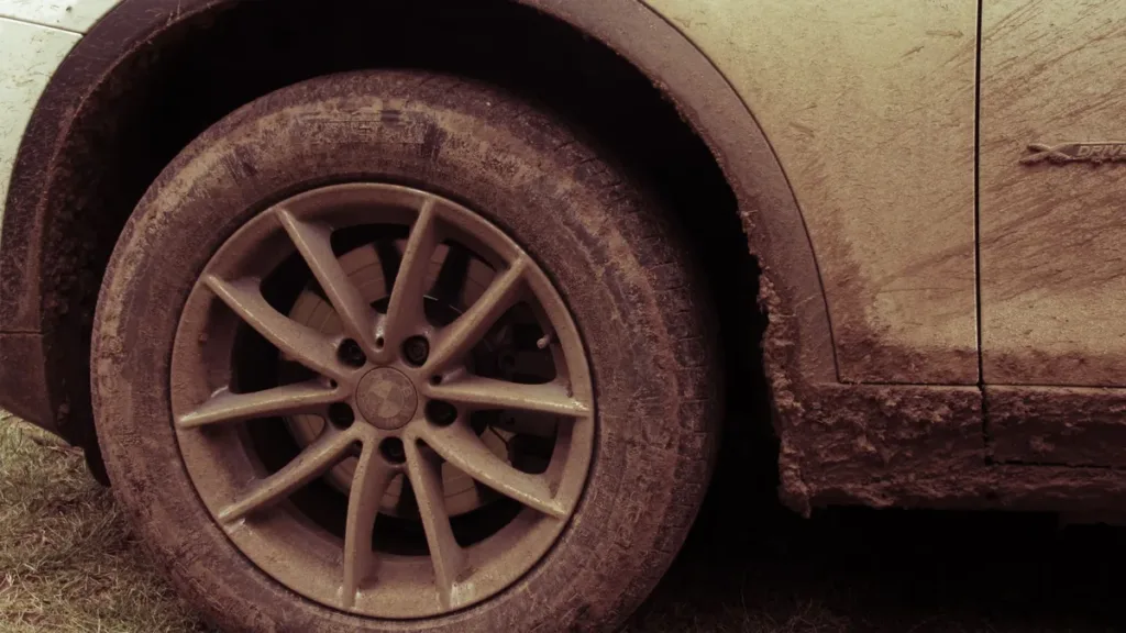 Dust- and mud-covered alloy wheel and tyre on a light-coloured car, the kind of grime that hides scratches