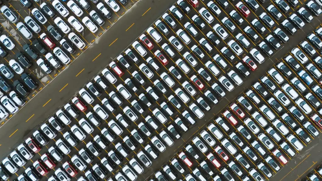 Aerial view of rows of mostly white and grey cars parked tightly on a large vehicle lot
