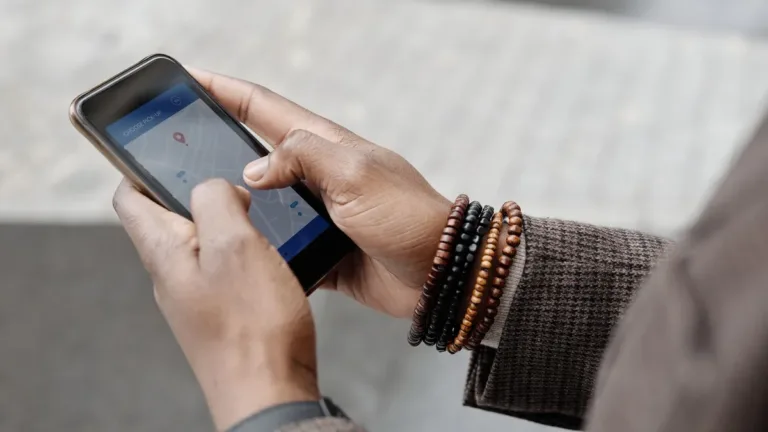 Close-up of two hands holding a smartphone with a map app open, a beaded bracelet on one wrist
