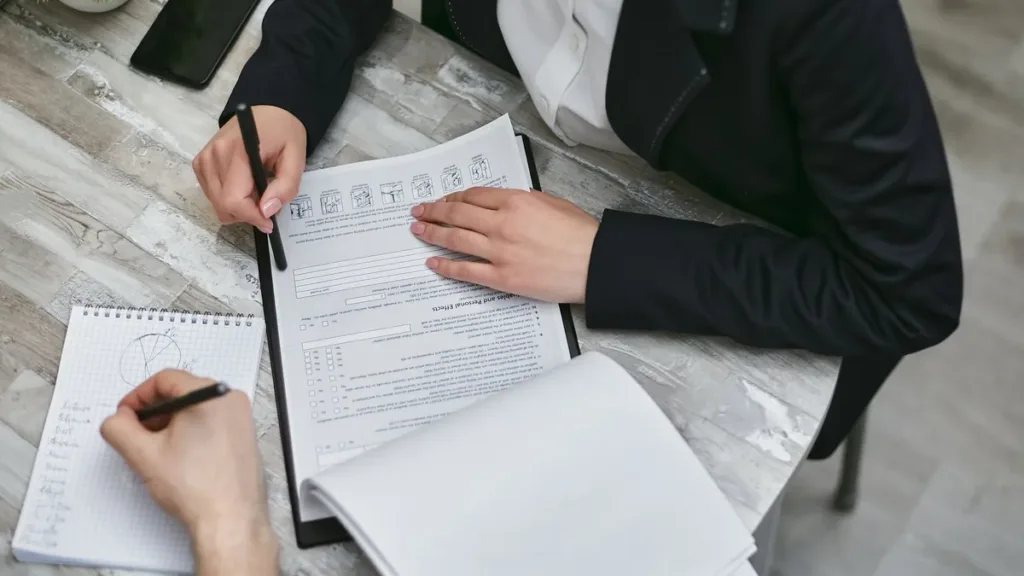 Overhead view of two people at a desk reviewing and annotating printed documents on a clipboard with pens
