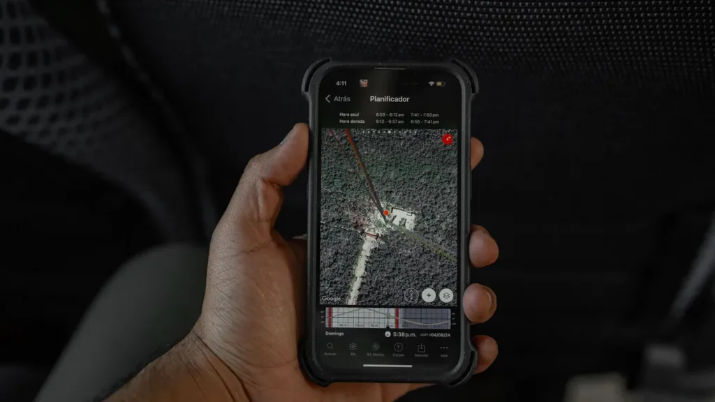 Hand holding a smartphone in a rugged case showing a satellite map view with a location marker, against a dark background