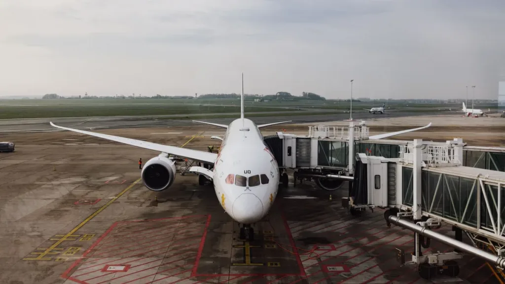 Unbranded passenger jet parked at an airport terminal gate with jet bridges attached under an overcast sky