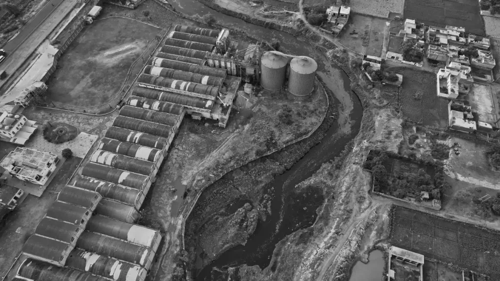 Black and white aerial view of factory sheds, storage tanks and a winding river channel in an industrial area of Punjab