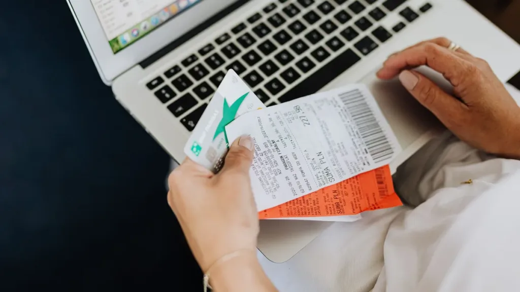 Hands holding a bank card and paper receipts in front of an open laptop, checking payment details