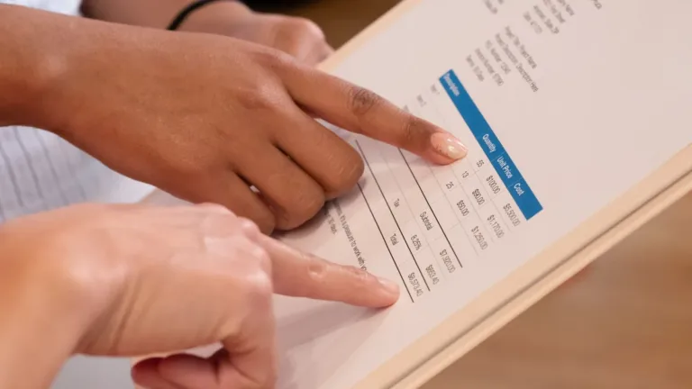 Two hands pointing at line items on a printed itemised document held on a clipboard