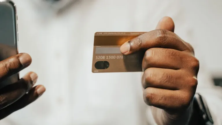 Hand holding a bank payment card beside a smartphone, ready to enter card details for an online payment