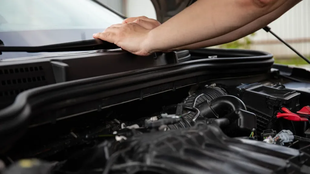 Hands resting on the raised bonnet of a car, with the engine bay and components visible below