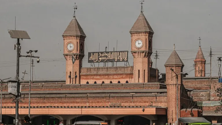 Red-brick clock towers of Lahore Junction railway station with cars, rickshaws and travellers on the forecourt