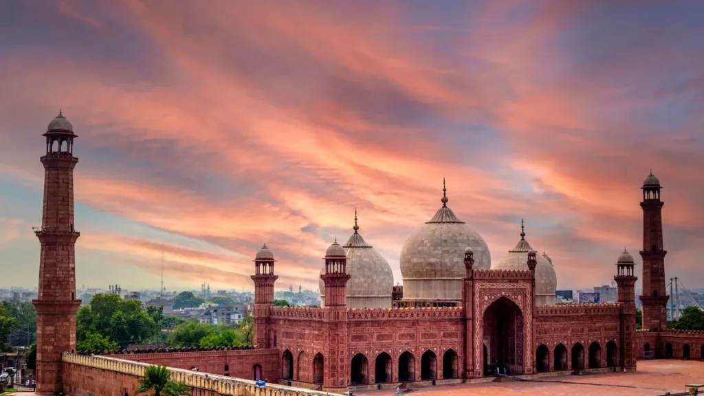 Badshahi Mosque in Lahore at sunset, red sandstone domes and minarets under a pink and orange sky