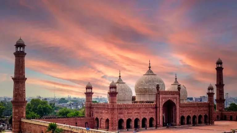Badshahi Mosque in Lahore at sunset, red sandstone domes and minarets under a pink and orange sky