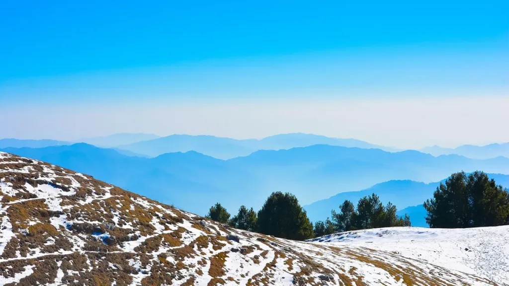 Snow-dusted hilltop with pine trees and layers of blue ridges beyond, in the Murree and Galyat hills of Pakistan