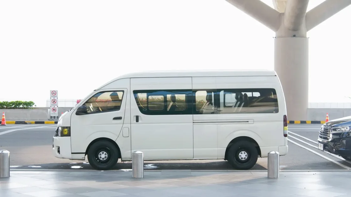 A white passenger minivan waiting at the drop-off kerb of a modern airport terminal under a canopy