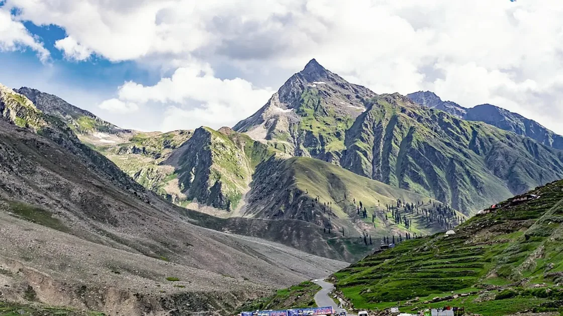 Vehicles on a mountain road through a green valley at Jalkhad near Naran, with steep peaks and white clouds