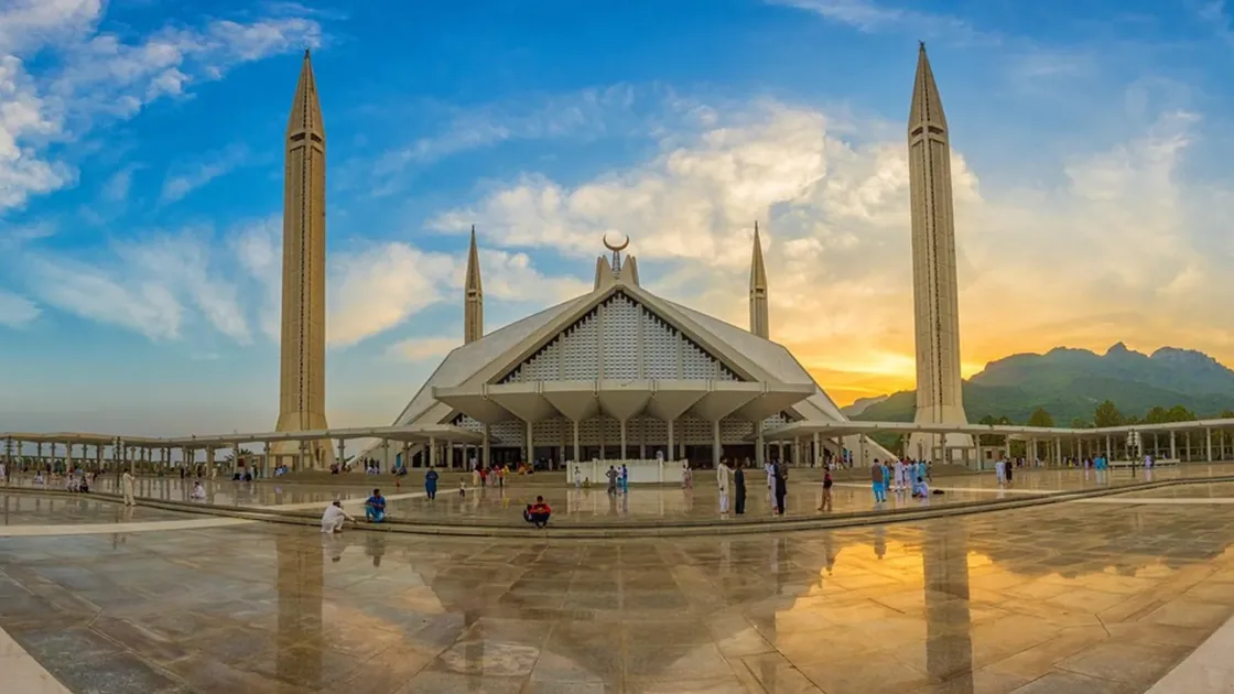 Panorama of Faisal Mosque in Islamabad at sunset, its courtyard reflecting the sky and the Margalla Hills