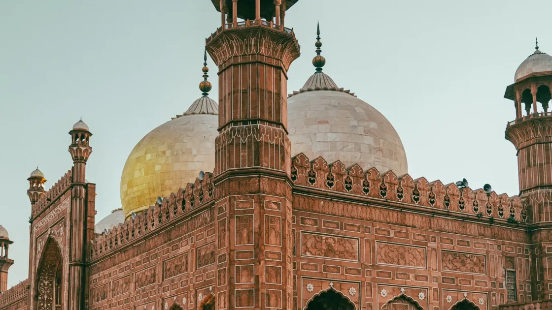 Badshahi Mosque in Lahore at dusk, its red sandstone walls, marble domes and minarets lit up