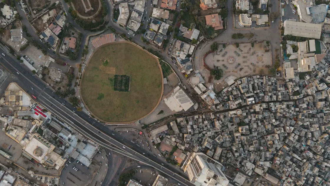 Aerial view of Karachi showing a main road with traffic curving past a circular park and dense city housing