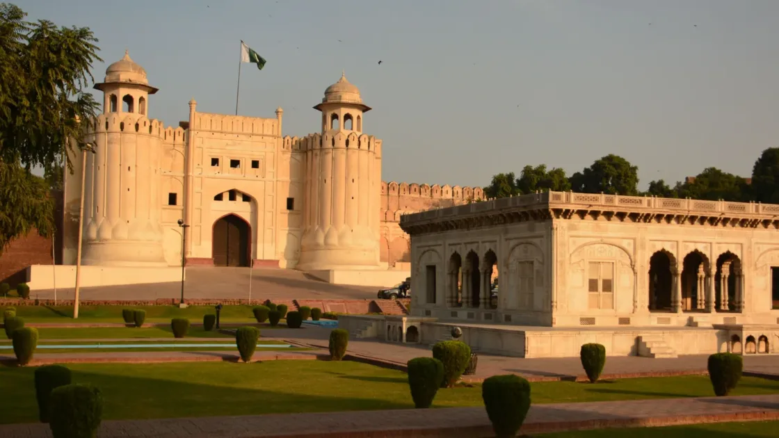 Alamgiri Gate of Lahore Fort and its gardens glowing in warm evening light, with a Pakistani flag above