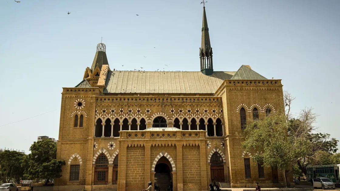 Frere Hall, the colonial-era sandstone landmark in Karachi, with a motorbike passing on the road in front