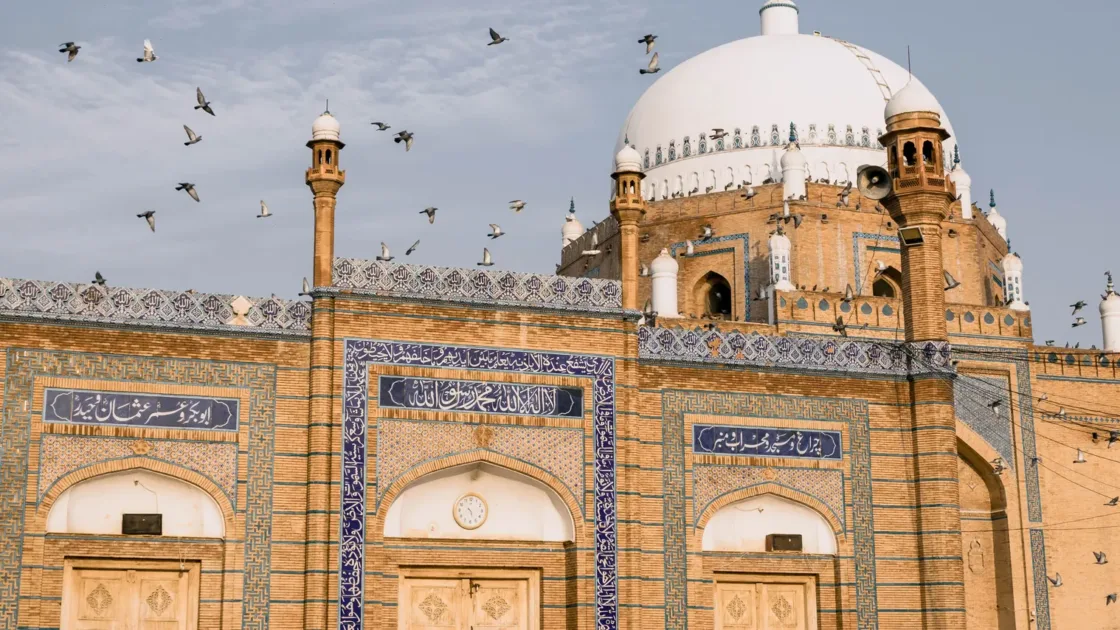 Shrine of Bahauddin Zakariya in Multan with its white dome, blue-tiled facade and pigeons in flight
