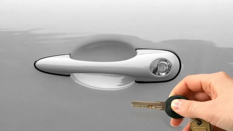 A hand holding a set of keys up to the chrome door handle and lock of a silver car, ready to unlock it