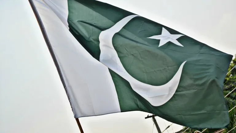 The green and white national flag of Pakistan with crescent and star flying from a pole above a street